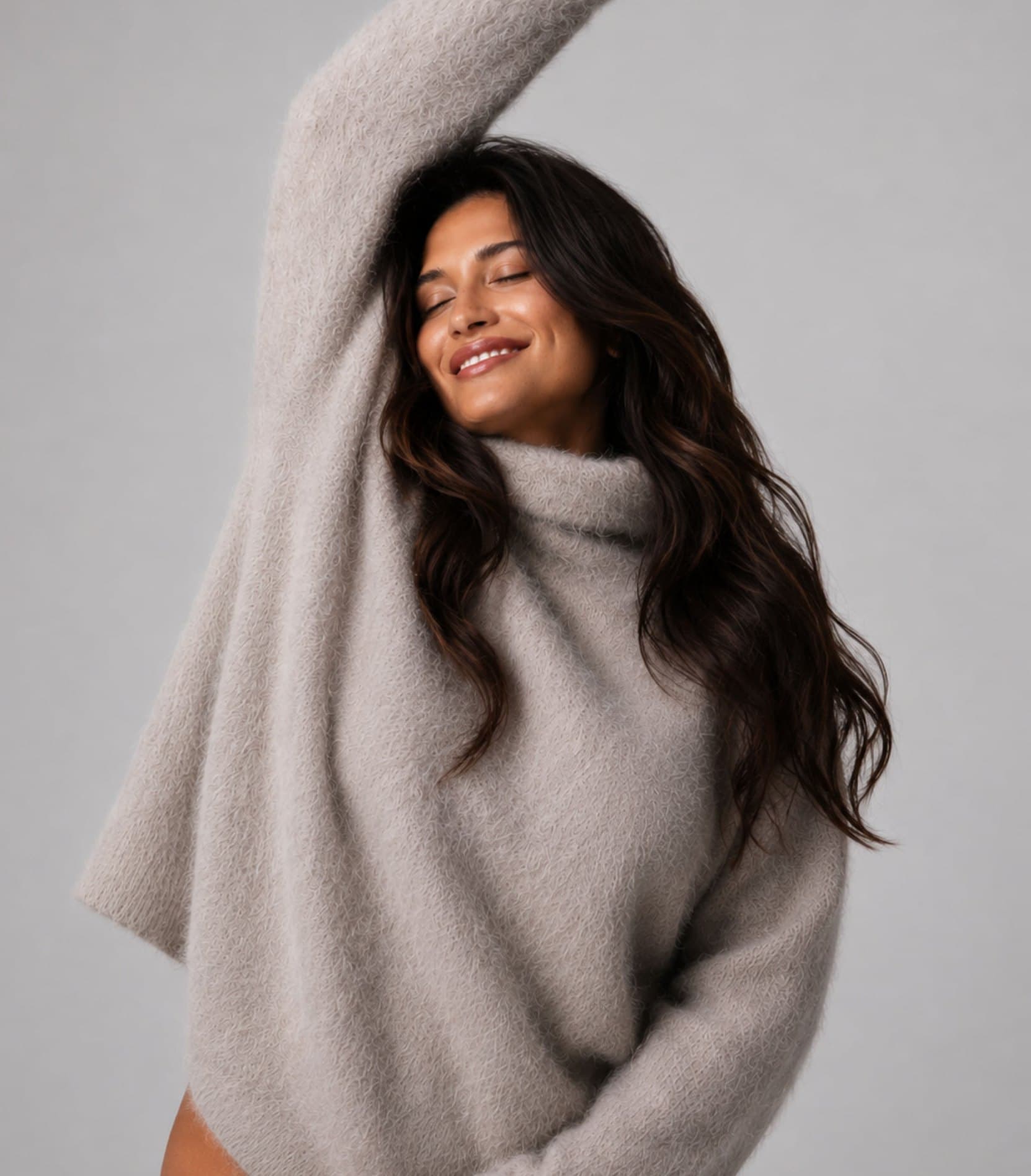 A woman in an oversized taupe sweater smiling with her arm raised