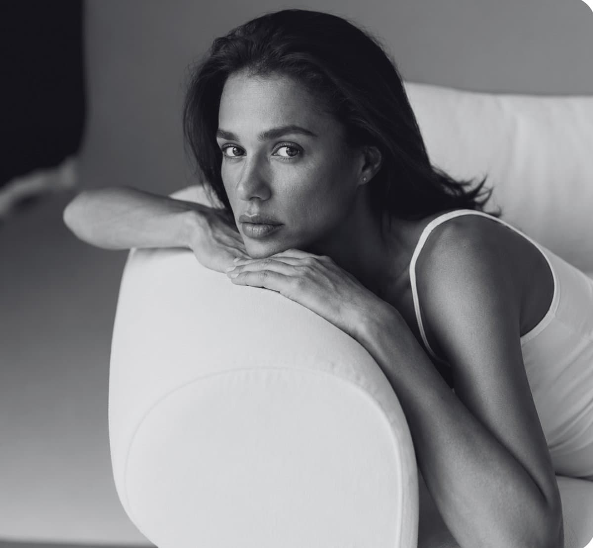 A woman resting her chin on her hands on the arm of a white sofa, black and white portrait