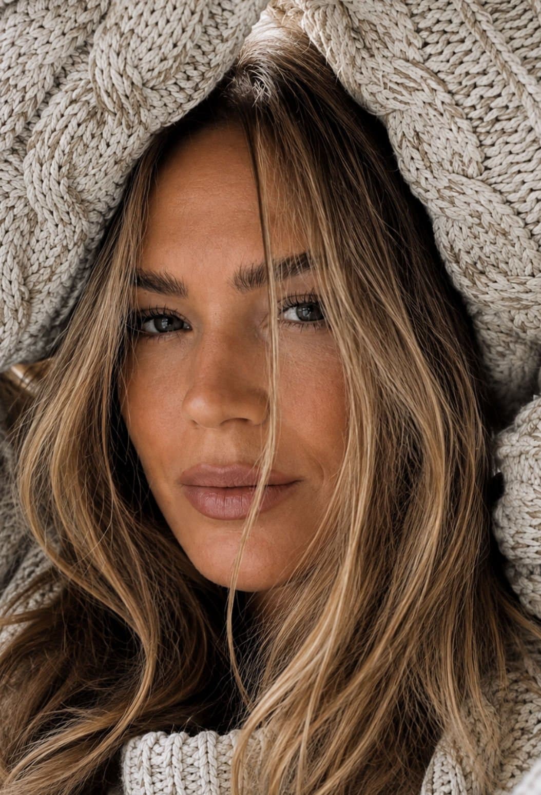 A close-up portrait of a woman wrapped in a cable-knit sweater