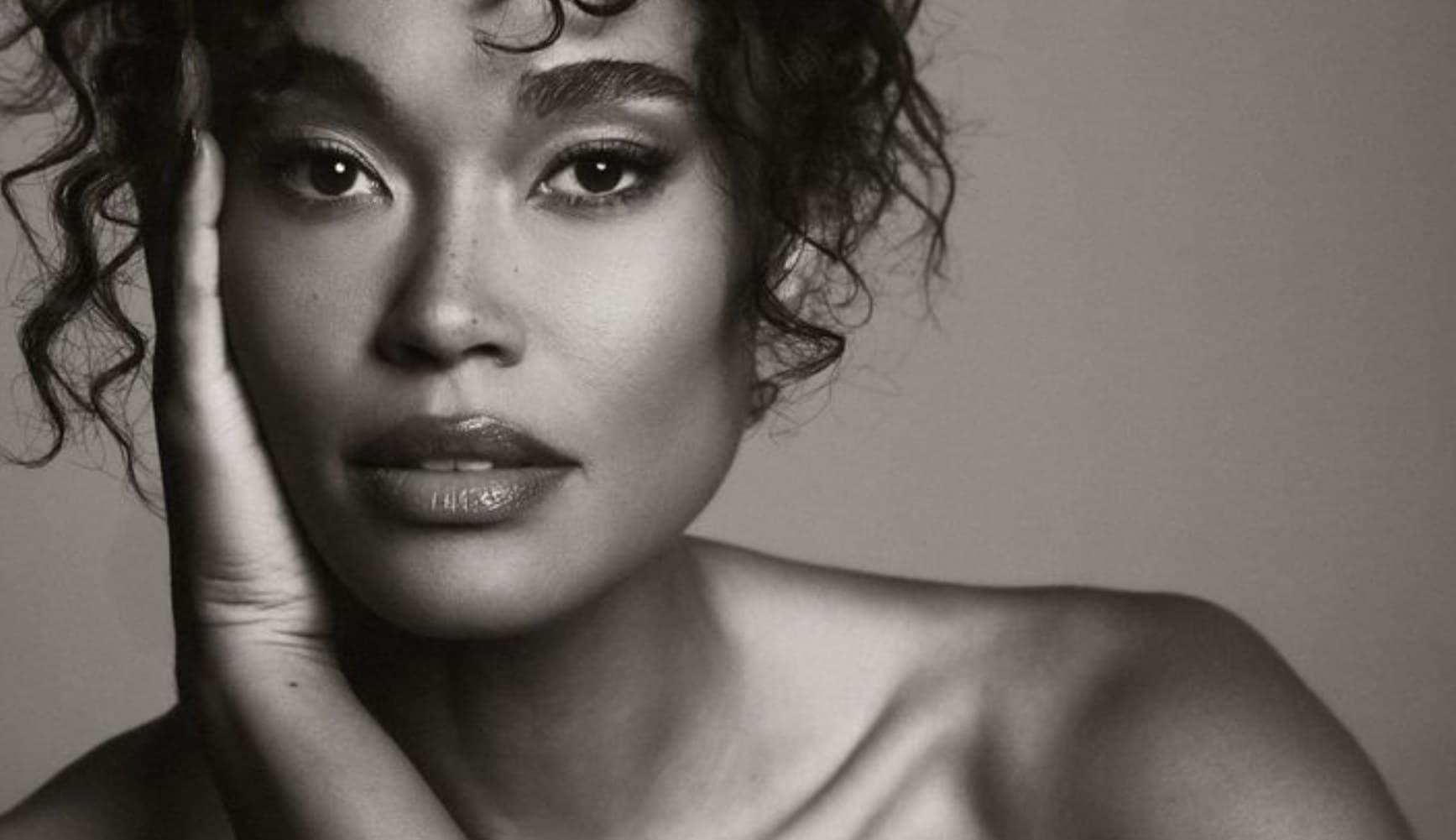 A woman with curly hair resting her hand against her cheek, black and white portrait