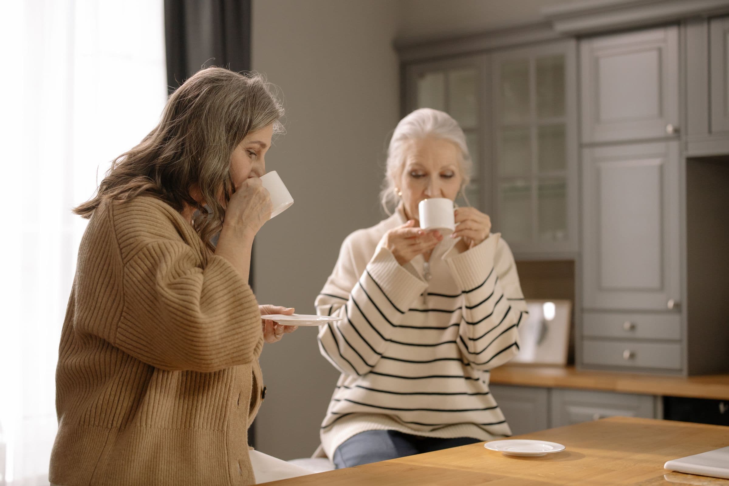 Two women sharing coffee at a kitchen table, opening a guide to combining a GLP-1 with HRT for menopause weight loss