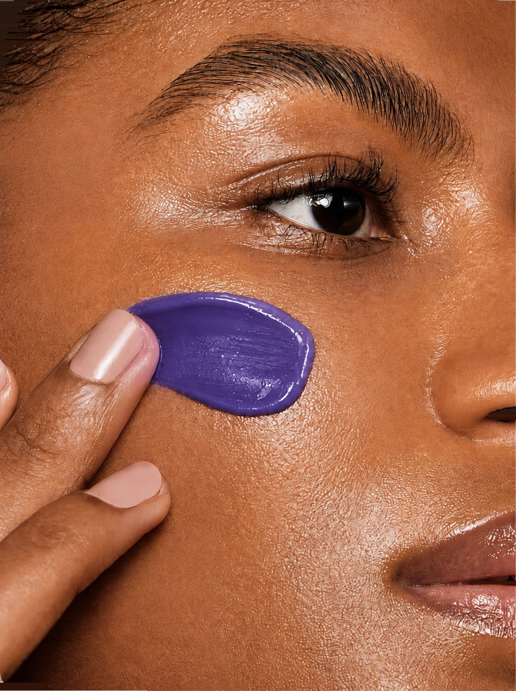 A woman pressing violet cream into her cheek