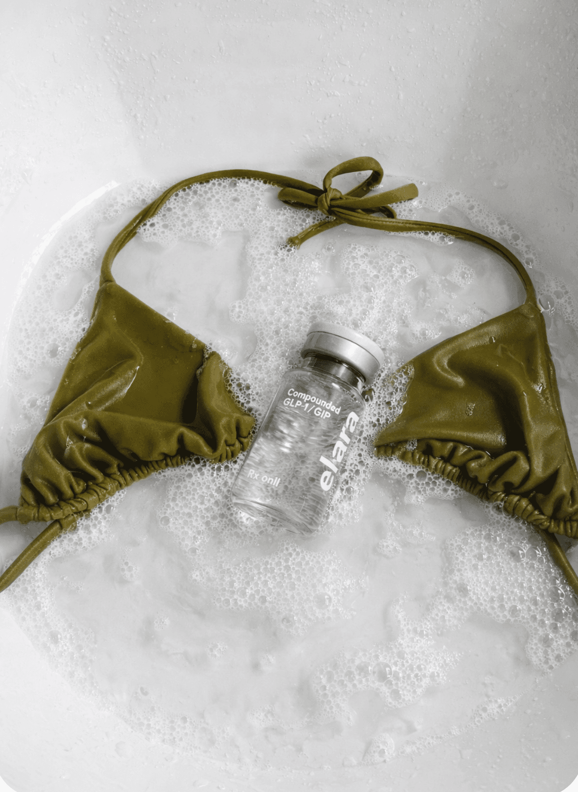 An elara vial resting on a swimsuit in bathwater