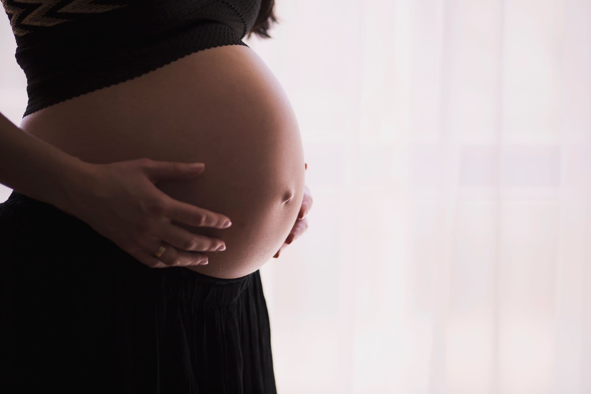 A pregnant woman resting her hands on her belly, opening a washout guide on when to stop semaglutide before conceiving