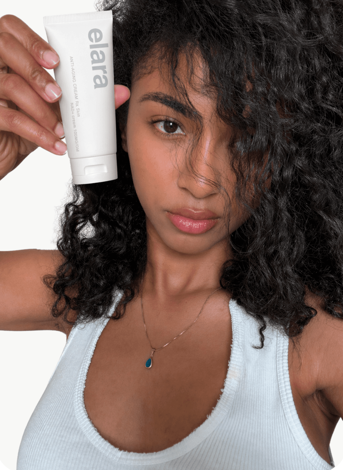 A woman holding an elara cream tube beside her face