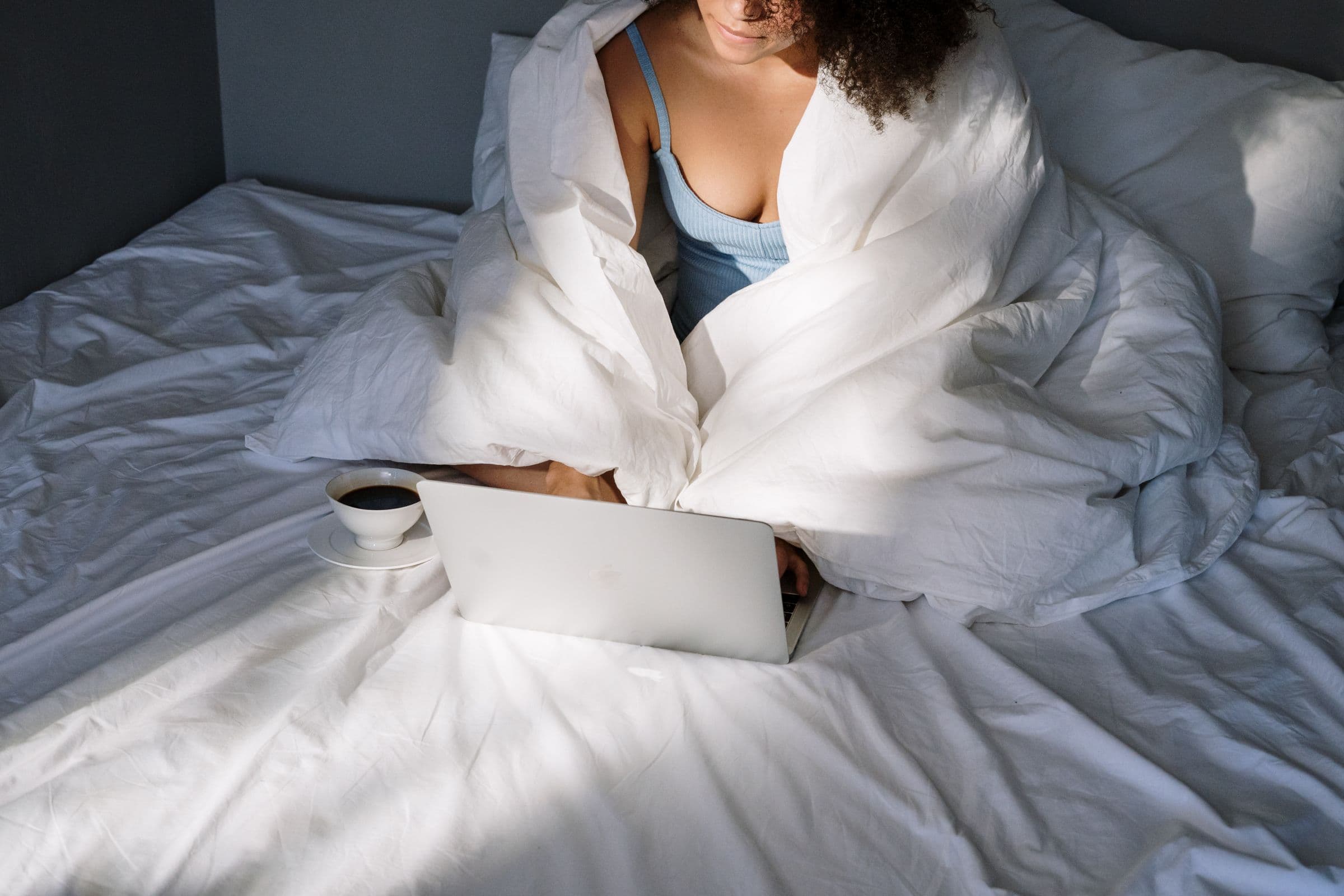 A woman reading on a laptop in bed while checking whether an online semaglutide provider is safe