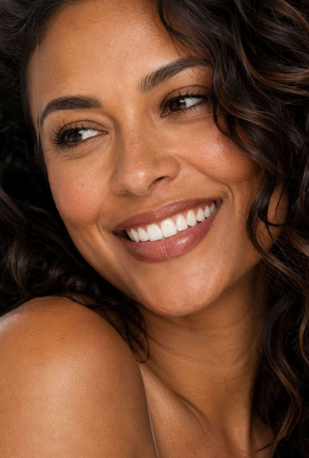 A smiling woman with curly hair, looking over her shoulder