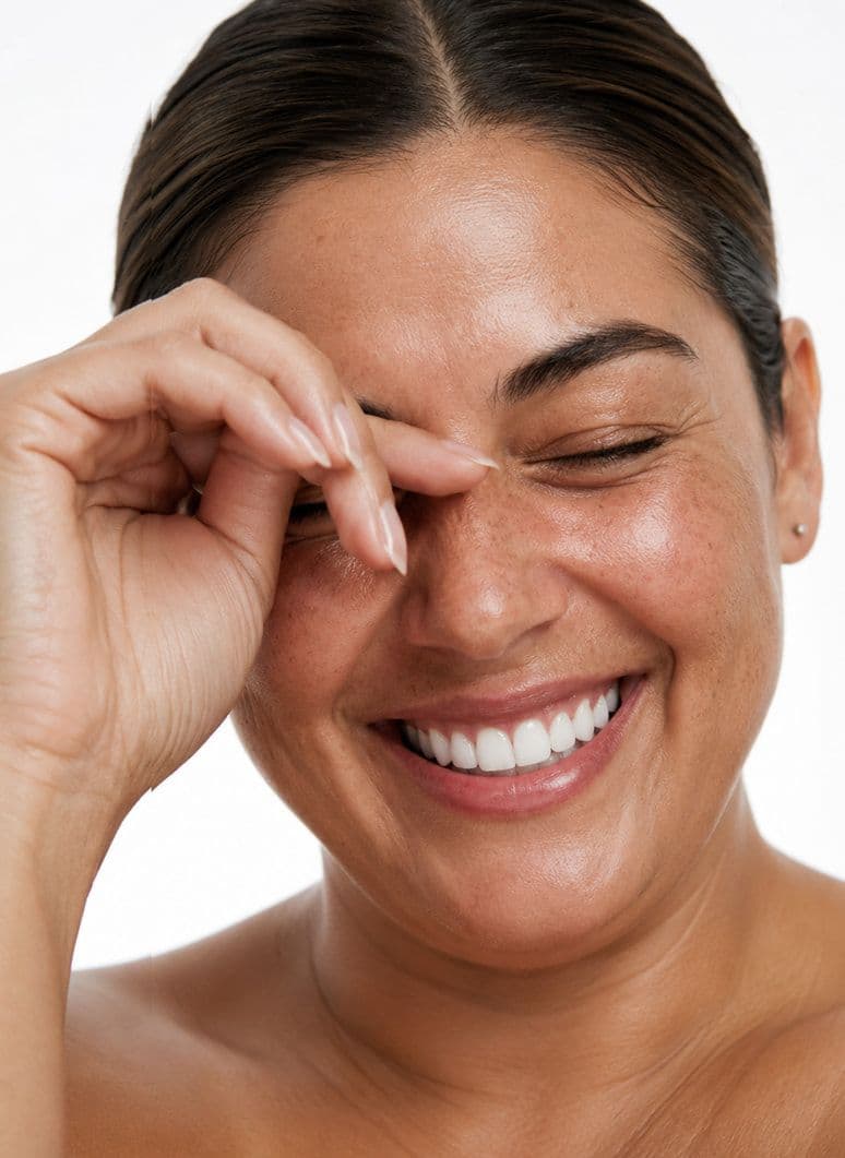 A woman laughing with her hand raised to her eye