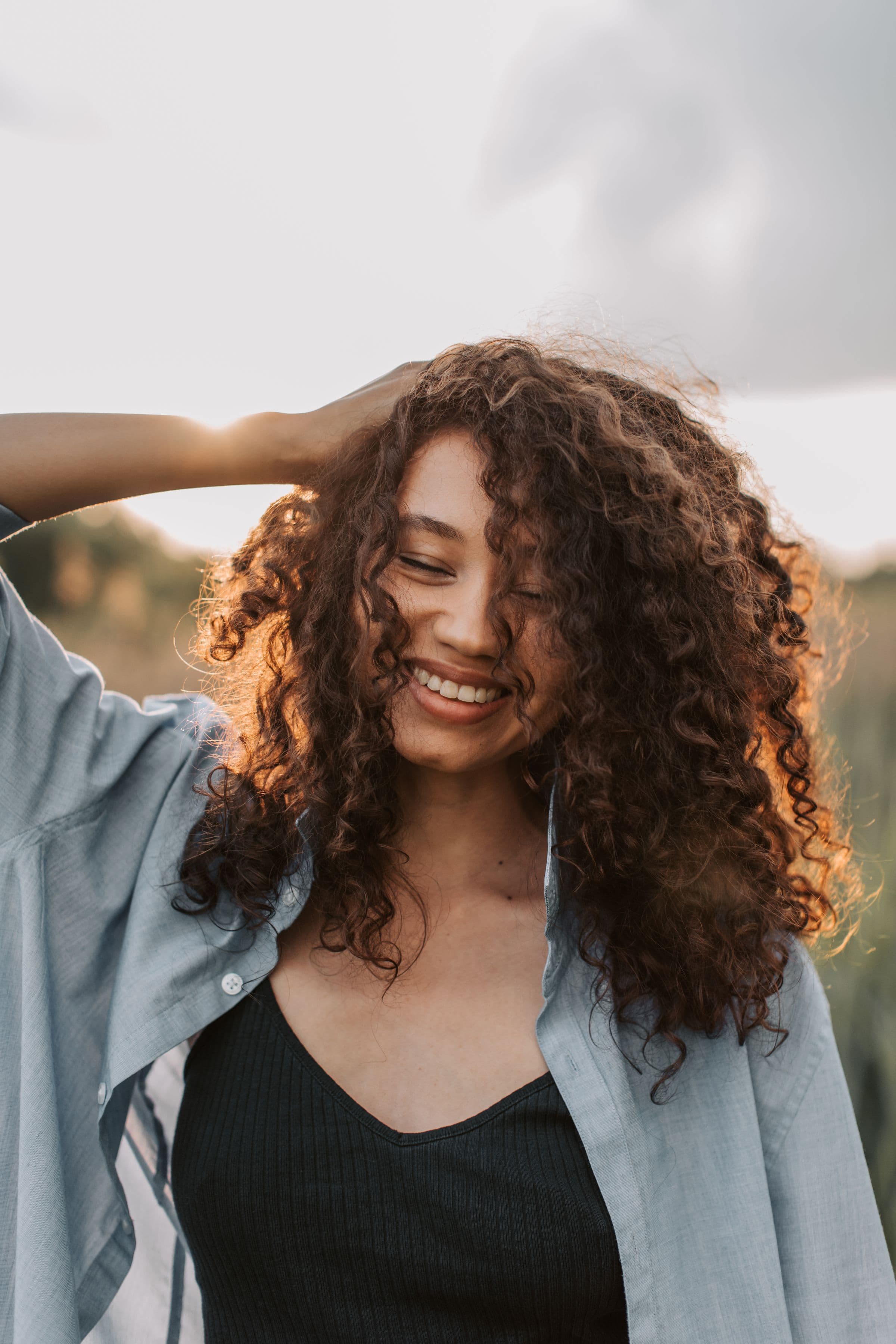 A woman with curly hair smiling outdoors, opening the question of whether semaglutide or tirzepatide changes your period