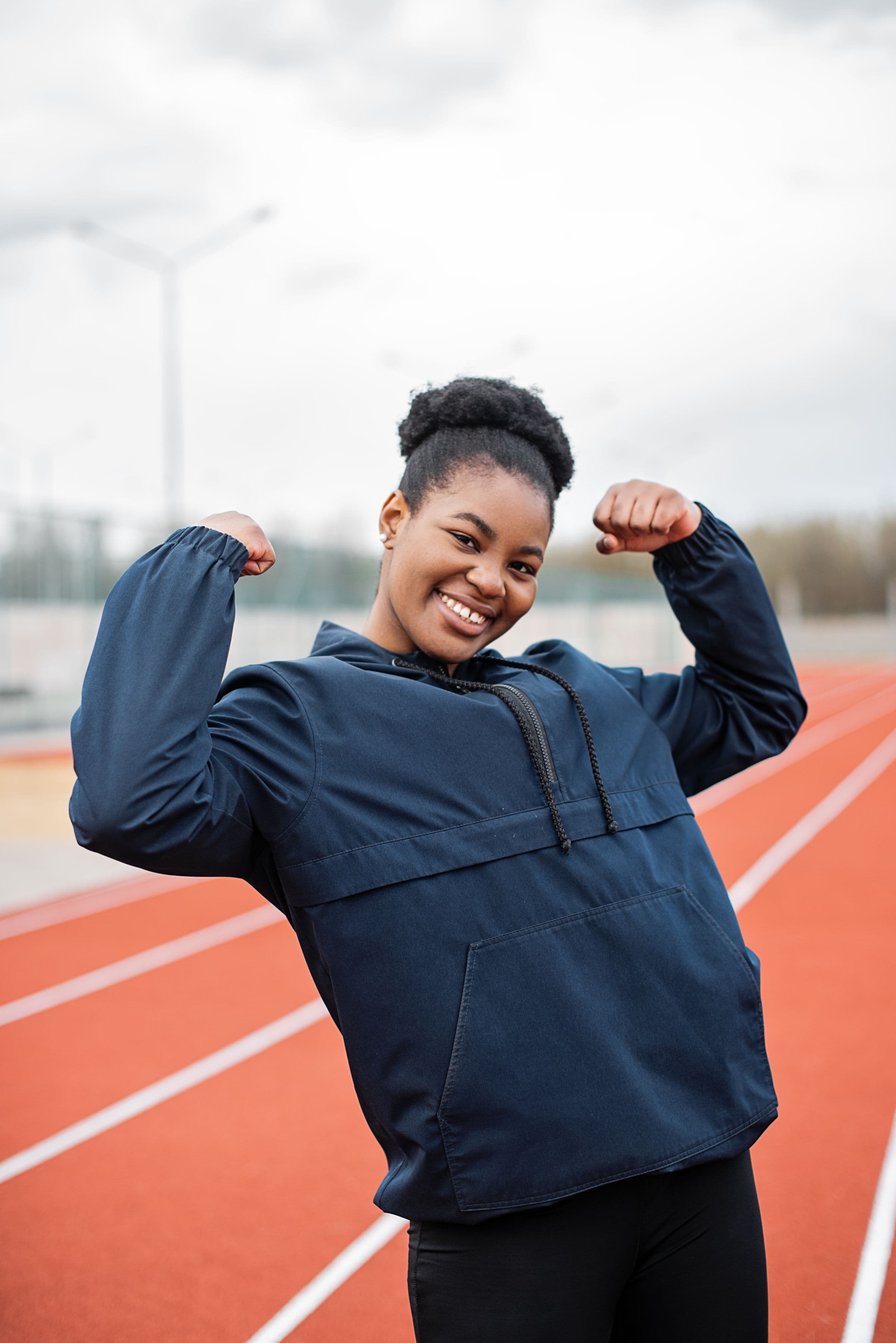 A smiling woman flexing both arms on a running track, opening a guide to how tirzepatide works for women