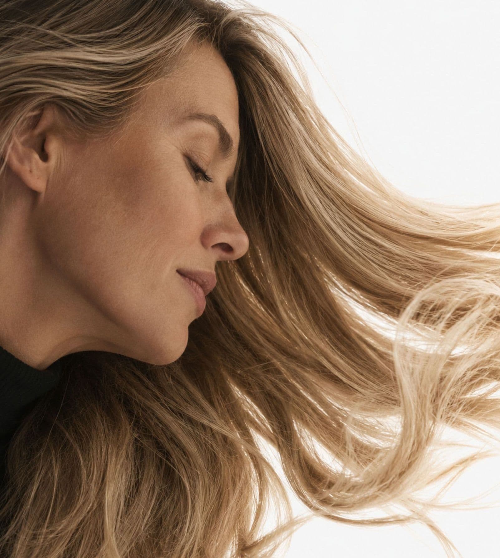A woman with long blonde hair, eyes closed, hair in motion