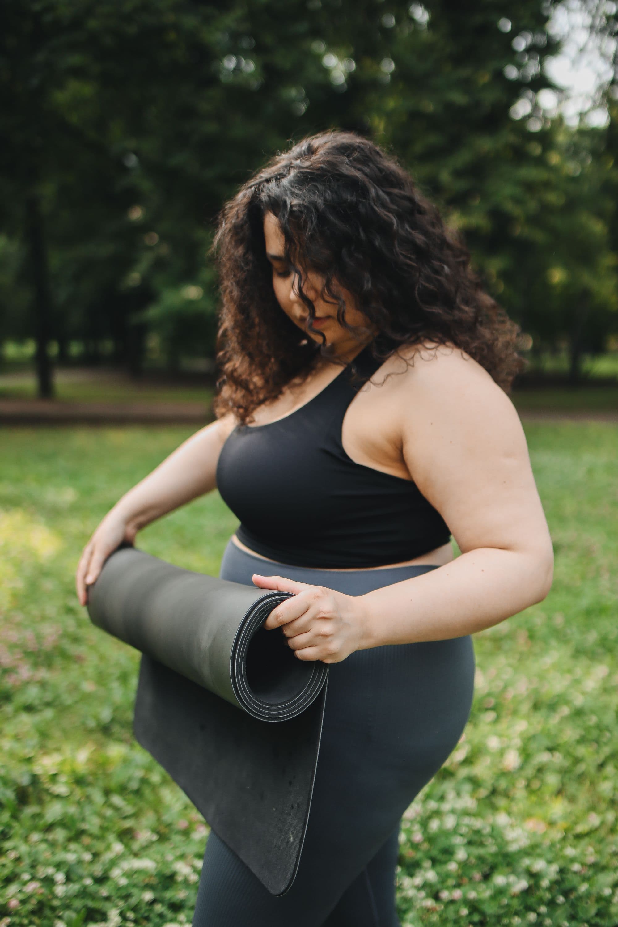 A woman in activewear holding a yoga mat in a park, opening a breakdown of what compounded tirzepatide costs
