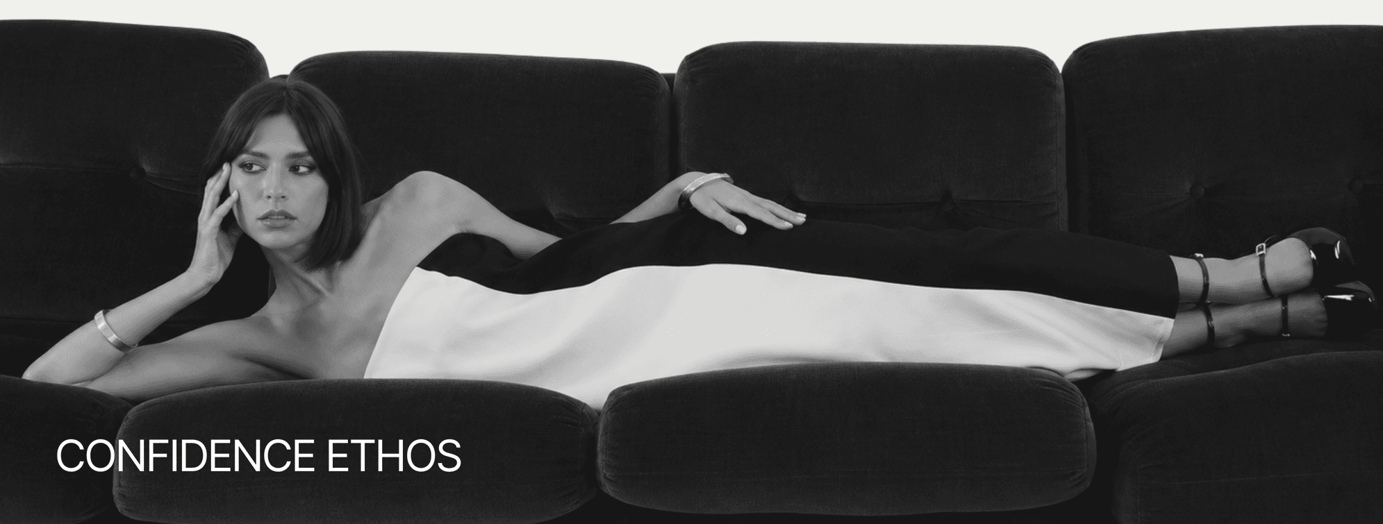 Confidence ethos: a woman in a black and white dress reclining on a dark velvet sofa