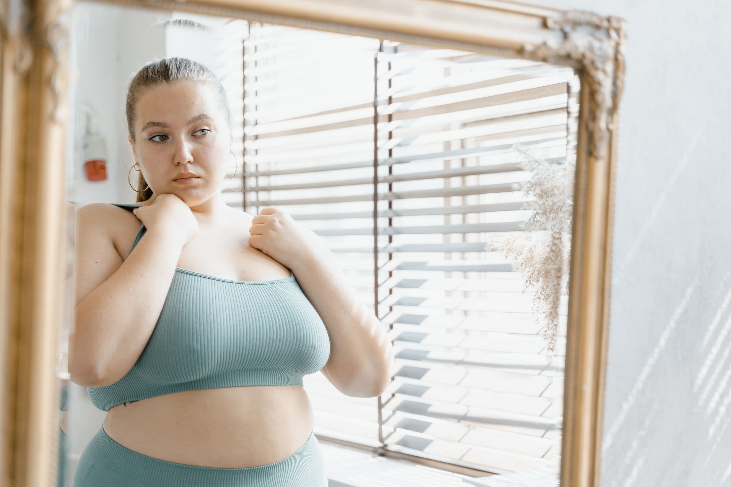 A woman in a sports bra studying her reflection, the moment of wondering why weight loss has stalled on semaglutide