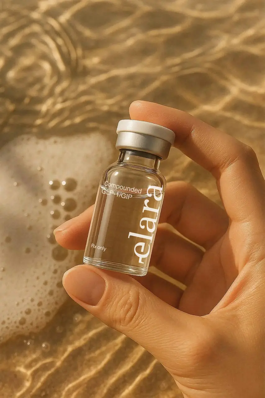 Hand holding an Elara branded compounded GLP-1/GIP medication vial above sand and foamy water